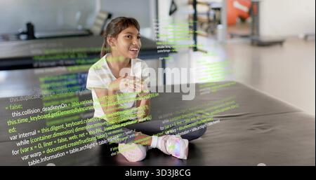 Sitting girl clasping hands on black mat in gym, wearing striped tee, pink shoes, code overlay Stock Photo
