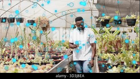 Walking mid-adult man in striped shirt and jeans, checking smartphone in greenhouse with succulents Stock Photo