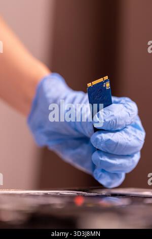 Technician wearing blue gloves using a screwdriver to repair or assemble a laptop’s internal components. Close-up of computer hardware maintenance Stock Photo