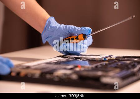 Technician wearing blue gloves using a screwdriver to repair or assemble a laptop’s internal components. Close-up of computer hardware maintenance Stock Photo