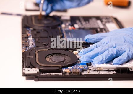 Technician wearing blue gloves using a screwdriver to repair or assemble a laptop’s internal components. Close-up of computer hardware maintenance Stock Photo