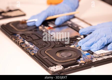 Technician wearing blue gloves using a screwdriver to repair or assemble a laptop’s internal components. Close-up of computer hardware maintenance Stock Photo