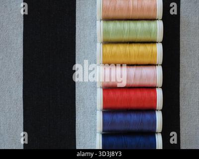 Top view of multicolored sewing threads on striped textile surface for fashion design and craft Stock Photo
