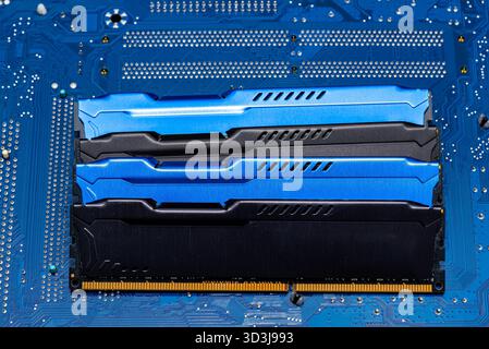 Four DDR memory chips in different colors lying on a blue printed circuit board. Stock Photo