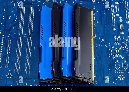 Four DDR memory chips in different colors lying on a blue printed circuit board. Stock Photo