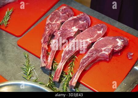 Food, Four raw tomahawk steaks arranged on a red cutting board with sprigs of fresh rosemary, ready for cooking or grilling Stock Photo
