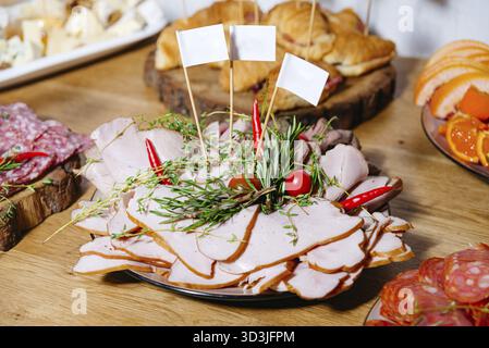 Food, Assorted sliced deli meats arranged on a serving platter with rosemary, thyme, cherry tomatoes, and red chili for catering event Stock Photo