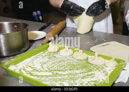 Food, Chef prepares traditional dumplings on a floured tray, stretching dough and forming filled pockets by hand in kitchen setting Stock Photo