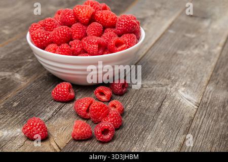 A white bowl of vibrant red berries on weathered grey wood. Stock Photo