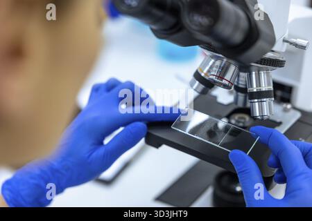 Unrecognizable scientist in blue surgical gloves working in laboratory, doctor using microscope analysis slides Stock Photo
