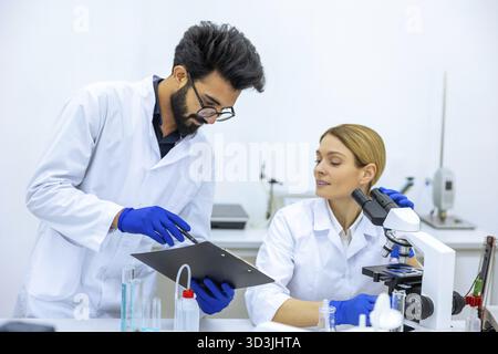 Woman and man scientists in lab coat making notes after doing sample test in laboratory, professional worker analyzes received data together Stock Photo