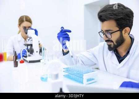 Team of scientists examining sample, female doctor using microscope, male researcher working with chemical liquids in flask in modern lab Stock Photo