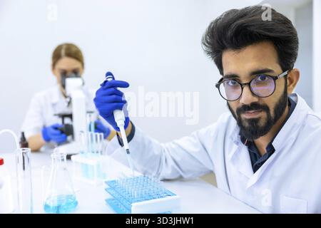 Team of scientists examining sample, female doctor using microscope, male researcher working with chemical liquids in flask in modern lab Stock Photo