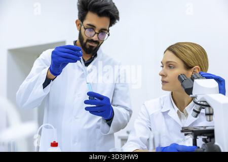 Young female and male scientists using pipette with test tube in medical science laboratory, researching medical sample blue liquid together Stock Photo