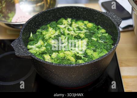 Food, Fresh broccoli florets boiling in a black speckled cooking pot on an induction stove, preparing a healthy vegetable dish Stock Photo
