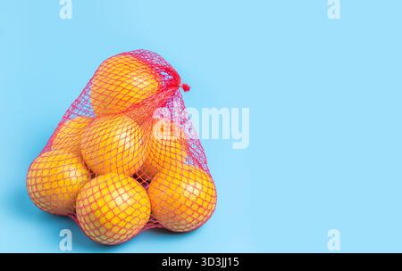 Grapefruit or oranges in a bright red net against a weathered gray wood background. Stock Photo