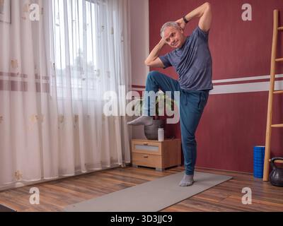 Senior man performing abdominal exercises on yoga mat in living room Stock Photo