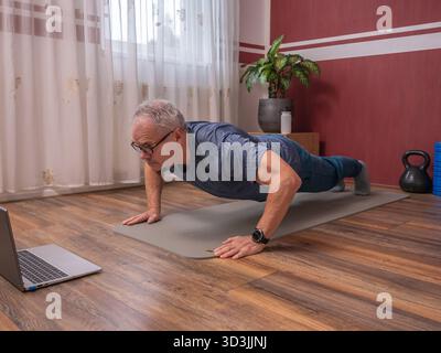 Senior man doing push-ups on yoga mat during home fitness training session Stock Photo