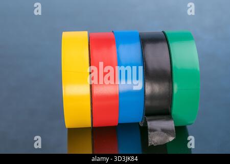 Five rolls of colorful electrical tape for repairs, on a reflective surface. Stock Photo