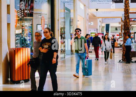 Young adult walking through a bright shopping mall corridor talking on a mobile phone and carrying a shopping bag. Stock Photo