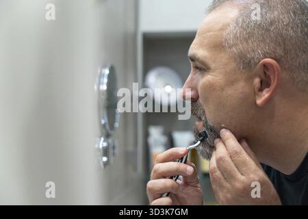 Middle-aged handsome man using razor in a bathroom Stock Photo