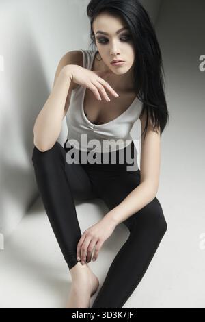 Cloe-up of black-haired model with make-up sitting on floor and looking up.Studio shot Stock Photo