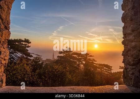 Mödling: mist at sunrise in Liechtenstein Castle Landscape Park, view through ruin Augengläser (Eyeglasses) to church Mödling, on mountain Kalenderber Stock Photo