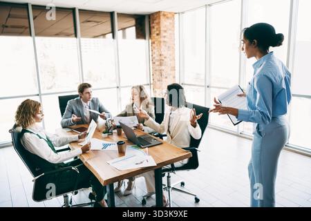 Diverse team collaborating in a workspace during a dynamic meeting, discussing projects and strategies in a bright office setting Stock Photo