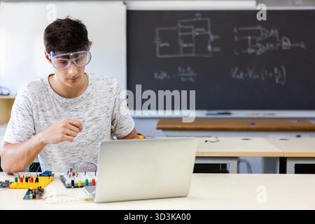 Young male student working on electronic experiment with laptop in classroom Stock Photo