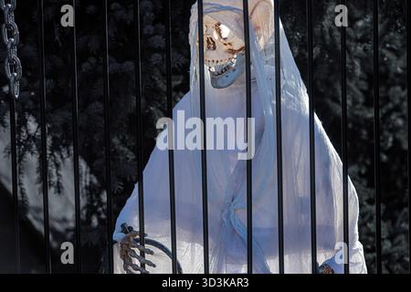 Skeleton figure dressed in white cloth behind black bars used as Halloween decoration in an outdoor setting Stock Photo