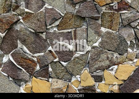 Irregular Stone Wall Texture Background. Close-up of a decorative wall made from uneven, natural stone pieces in earthy tones, creating a rough and Stock Photo