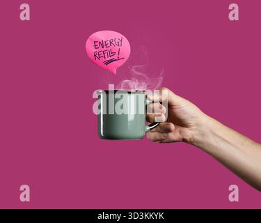 A Caucasian man's hand holds a steaming green enamel mug of coffee or tea with an "Energy Refill!" speech bubble, isolated on a vibrant pink backgroun Stock Photo
