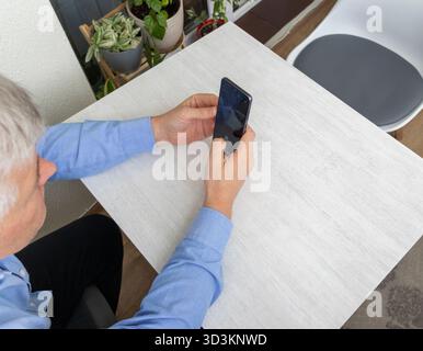 Mid aged man sitting at the table, using phone Stock Photo