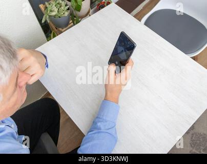 Mid aged man sitting at the table, using phone Stock Photo