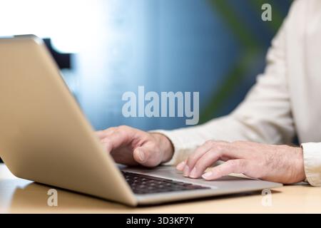 Close-up photo of the hands of a young man in a shirt working and typing on a laptop keyboard. Stock Photo