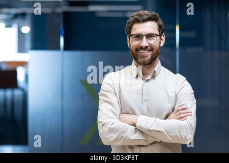 Portrait of a young programmer and engineer standing in the office with his arms crossed on his chest and smiling at the camera. Stock Photo