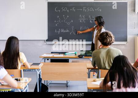 Female teacher explaining chemistry formulas on blackboard to high school students Stock Photo