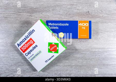 Boxes of amoxicillin 500mg antibiotic capsules and metronidazole 400mg tablets placed on a gray wooden surface oral medication for bacterial infection Stock Photo