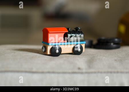 Wooden toy train with red roof and black engine sits on fabric surface, showcasing classic design and vibrant colors. Stock Photo