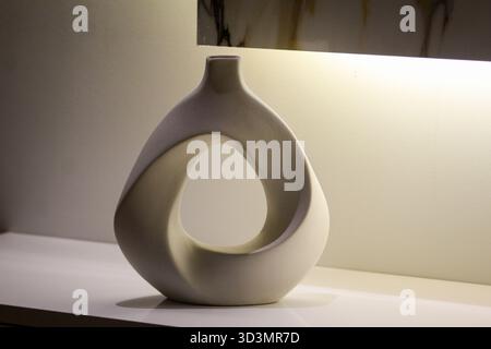 Stylish white ceramic vase with an open geometric design placed on a white surface, illuminated by soft indoor light. Stock Photo