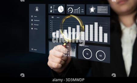 A business professional interacts with a futuristic touchscreen display, analyzing statistical data and trends with a magnifying tool for enhanced Stock Photo