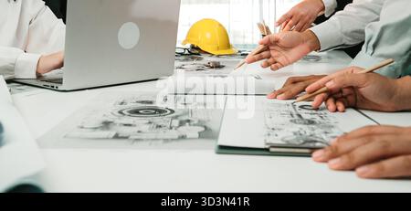 A collaborative meeting taking place in a modern office, showcasing hands actively engaged in design discussions, with a laptop and sketches spread Stock Photo
