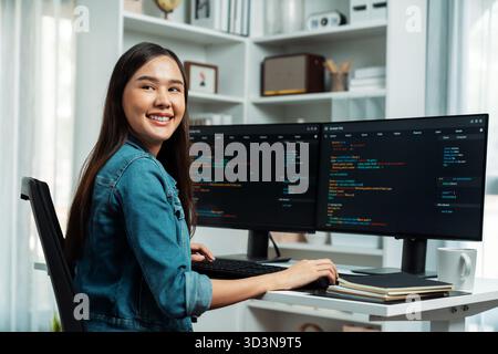 Young Asian in IT developer looking at camera to present with online information on pc with coding program data application, wearing jeans shirt Stock Photo