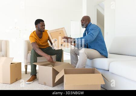 African American father and son unpacking moving boxes in living room, with wooden picture frame Stock Photo