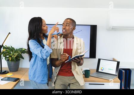 Discussing African American professionals analyzing data on office desk, with monitor and laptop Stock Photo