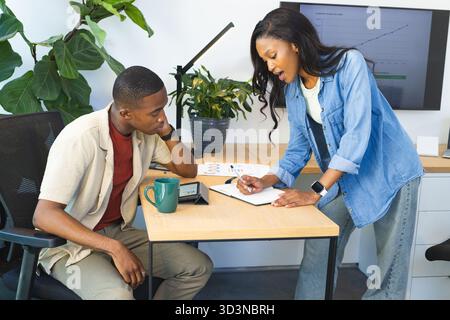 Collaborating African American colleagues reviewing graph on office desk, with notebook and tablet Stock Photo