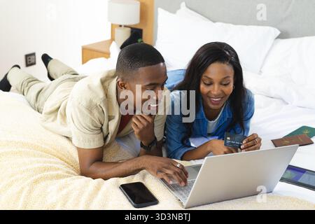 Reclining African American couple using laptop in bright bedroom, with passports and tablet Stock Photo