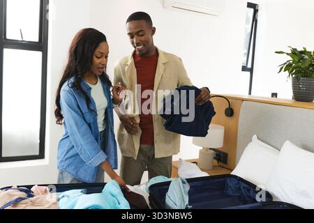 Packing African American couple organizing suitcase on bed in modern bedroom, with folded clothes Stock Photo