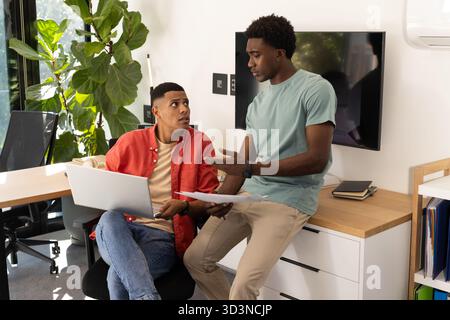 Diverse male coworkers discussing documents in modern office, using laptop on desk Stock Photo