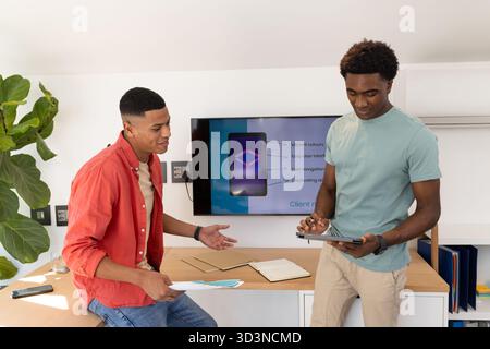 Collaborating Diverse male colleagues discussing design on desk in office, with tablet and papers Stock Photo